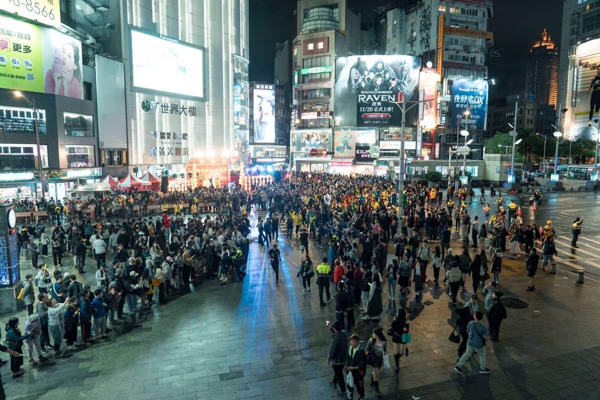 Nächtliche Szene in Ximending mit einer großen Menschenmenge in der Fußgängerzone, umgeben von leuchtenden Werbetafeln und belebten Gebäuden.