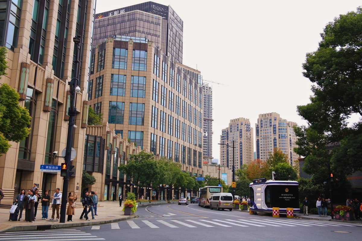 Weitwinkelansicht der Huaihai Road in Xintiandi, Shanghai, mit modernen beigefarbenen Bürogebäuden, Bussen und wartenden Fußgängern an der Straße.