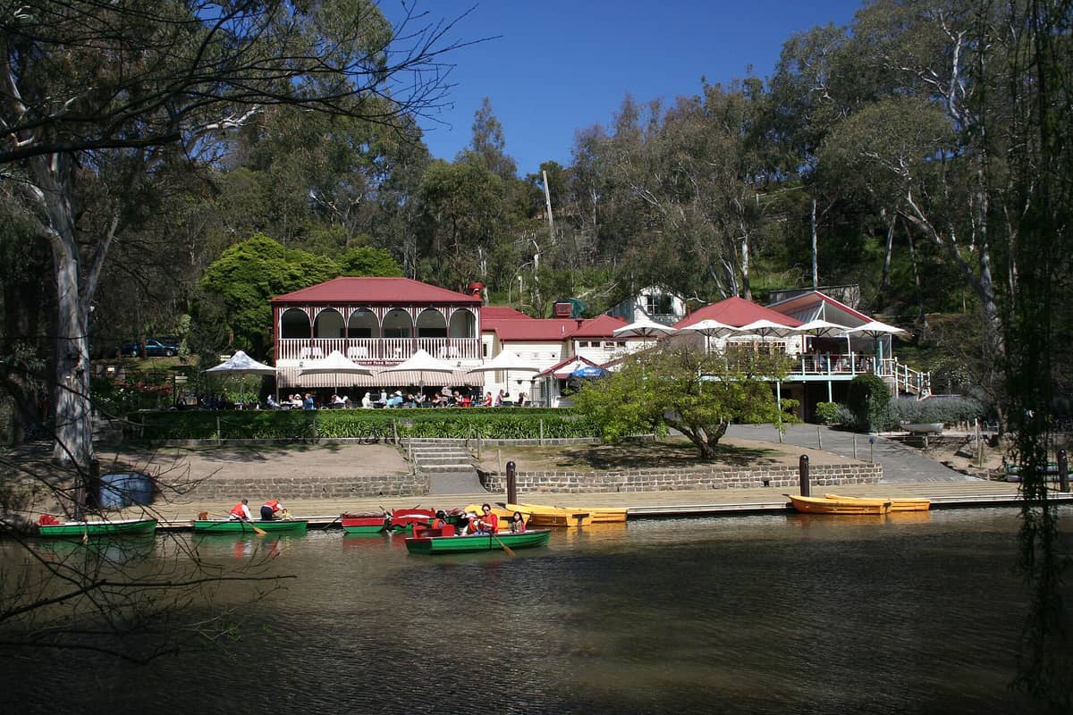 Das Bootshaus im Yarra Bend Park am Yarra River mit Ruderbooten, umgeben von einheimischem Buschland und Bäumen unter einem klaren blauen Himmel.
