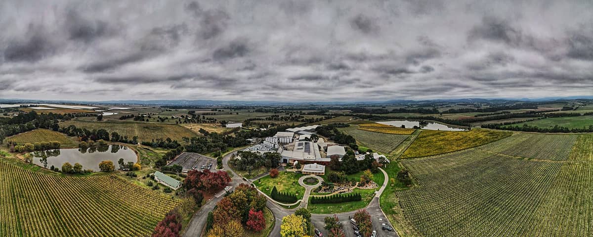 Vista aérea de los viñedos del Yarra Valley con bodegas, pequeños lagos, campos ondulados y cielos nublados dramáticos en Victoria, Australia.