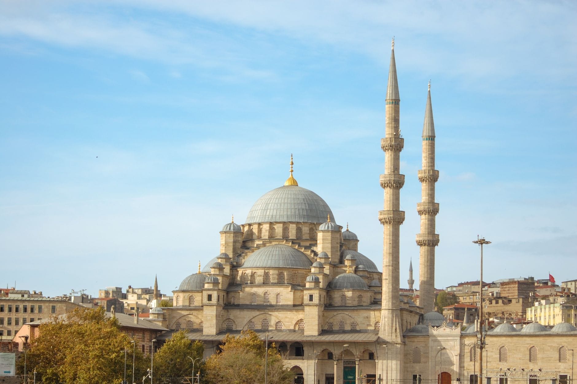 Vista panoramica della Yeni Cami (Moschea Nuova) con le sue grandi cupole e i due minareti che si stagliano sul vivace quartiere di Eminönü sotto un cielo azzurro e sereno.