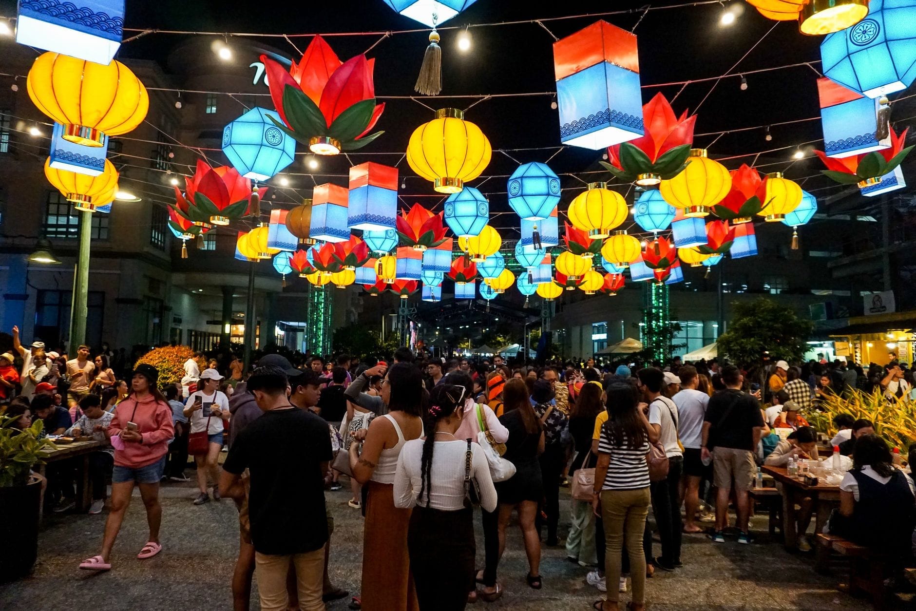 Con phố đông đúc ở Chiang Mai vào ban đêm, được trang trí bằng những chiếc đèn lồng đầy màu sắc treo lơ lửng và nhộn nhịp người qua lại trong một lễ hội.
