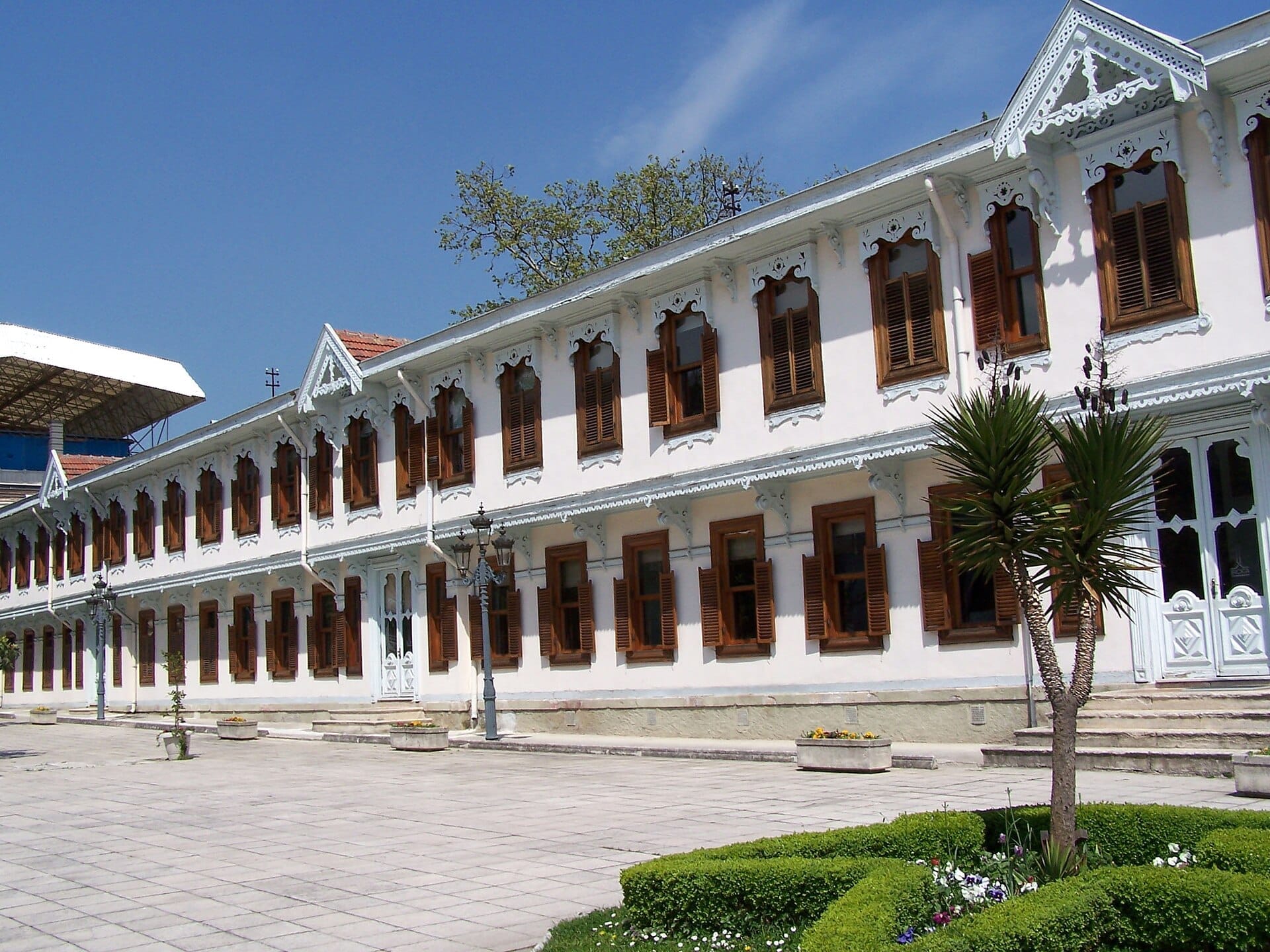 Edificio principale del Yıldız Palace con facciata bianca, persiane in legno e finiture ornate, circondato da giardini paesaggistici sotto un cielo azzurro brillante.
