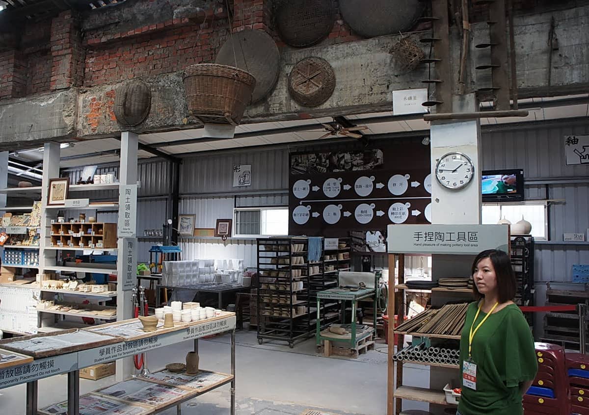 Innenansicht des Keramikmuseums in der Yingge Ceramics Old Street mit Töpferwerkzeugen, Regalen mit Waren und einem Besucher neben einem Schild.