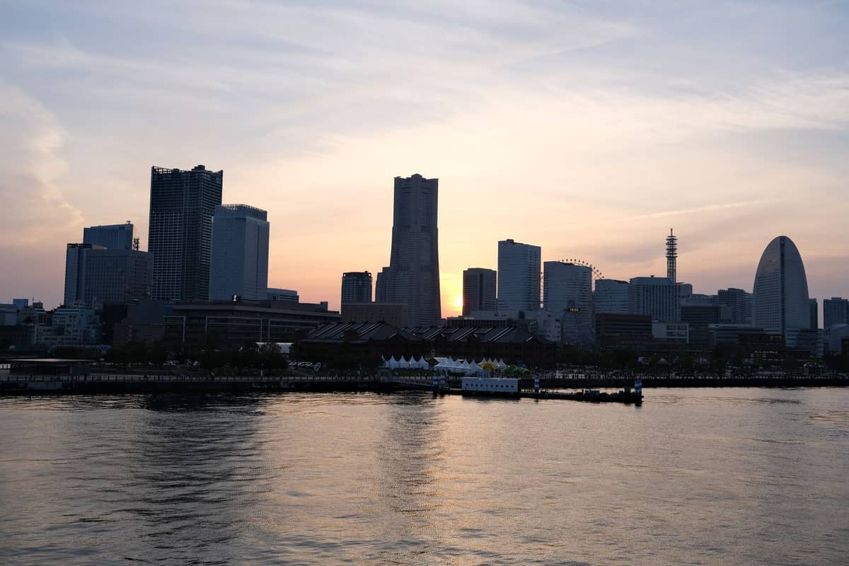 Silhouette of Yokohama's Minato Mirai skyline at sunset with Landmark Tower, waterfront, and ferris wheel seen across the bay.
