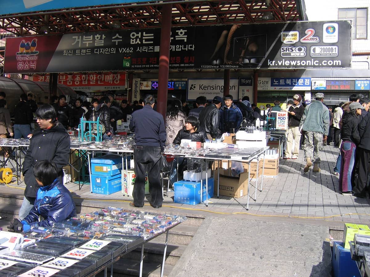 Compradores percorrem barracas externas de vendedores com peças eletrônicas e gadgets sob as toldos do mercado no Yongsan Electronics Market em Seul em um dia ensolarado.