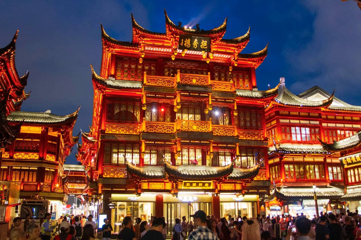 Nächtlicher Blick auf die beleuchteten traditionellen chinesischen Gebäude und das geschäftige Treiben am Yuyuan-Basar in Shanghais Altstadtviertel.