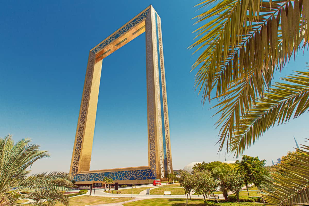 Der Dubai Frame ragt über Palmen und grüne Rasenflächen im Zabeel Park unter einem strahlend blauen Himmel auf.