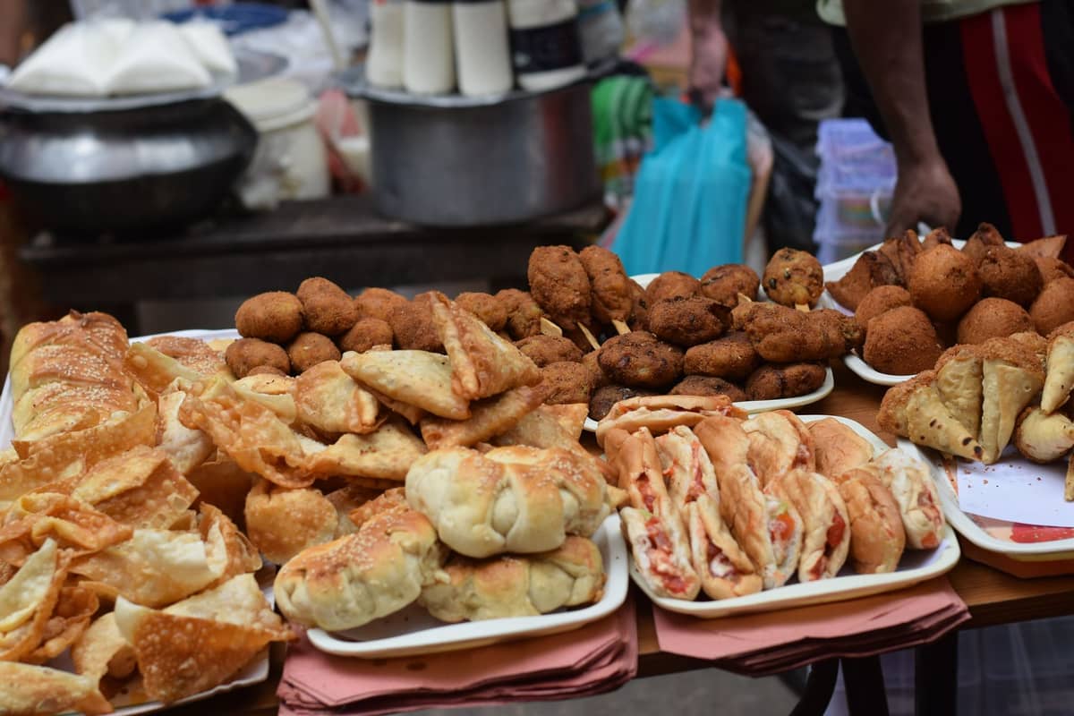 Piring-piring yang ditumpuk dengan berbagai camilan goreng dan kue di meja lapak makanan jalanan.