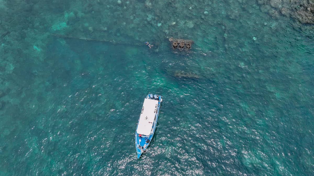 Vista aérea de un barco de snorkel anclado en aguas turquesas sobre un arrecife de coral frente a Zanzíbar, con practicantes de snorkel visibles en el mar cristalino.