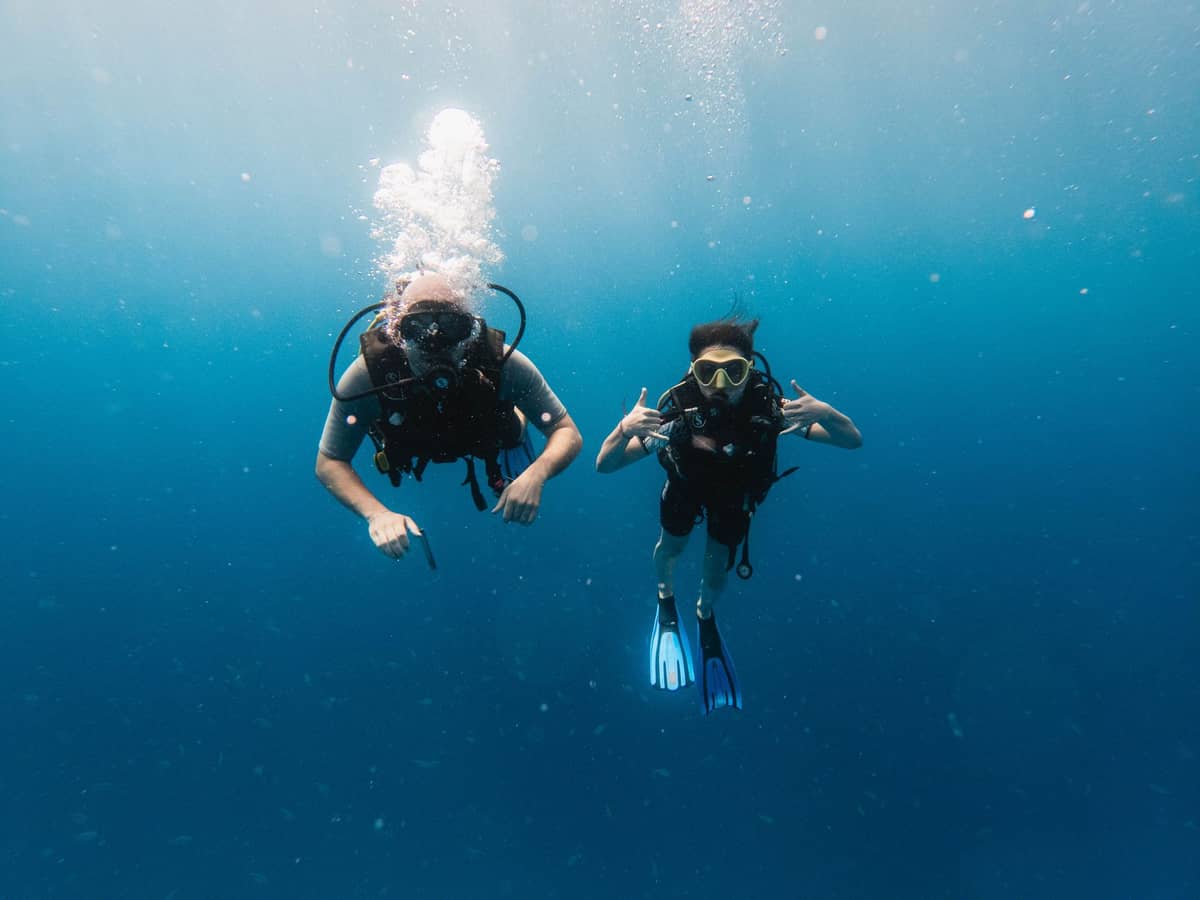 Dwóch nurków pod wodą w krystalicznie błękitnym oceanie, ilustrujących doświadczenie nurkowania na Zanzibarze.