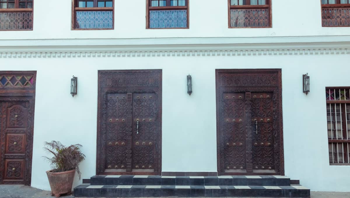 Widok frontowy białego budynku w Stone Town z dwojgiem okazałych rzeźbionych drewnianych drzwi w stylu zanzibarski — z misternym zdobieniem i tradycyjnymi mosiężnymi ćwiekami.