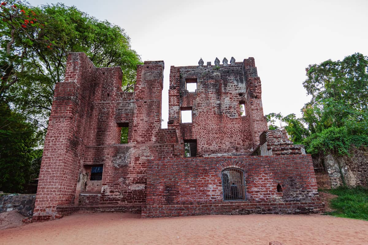Ruiny pałacowej budowli z czerwonej cegły otoczonej drzewami i piaskiem, prawdopodobnie zapomniane miejsce historyczne na Zanzibarze.