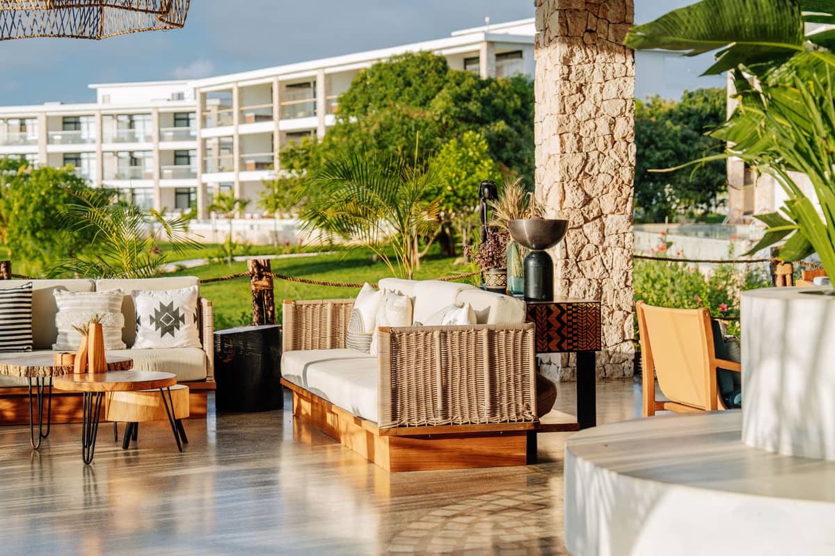 Outdoor lounge area of a tropical resort hotel with modern seating, palm trees, and a large hotel building in the background