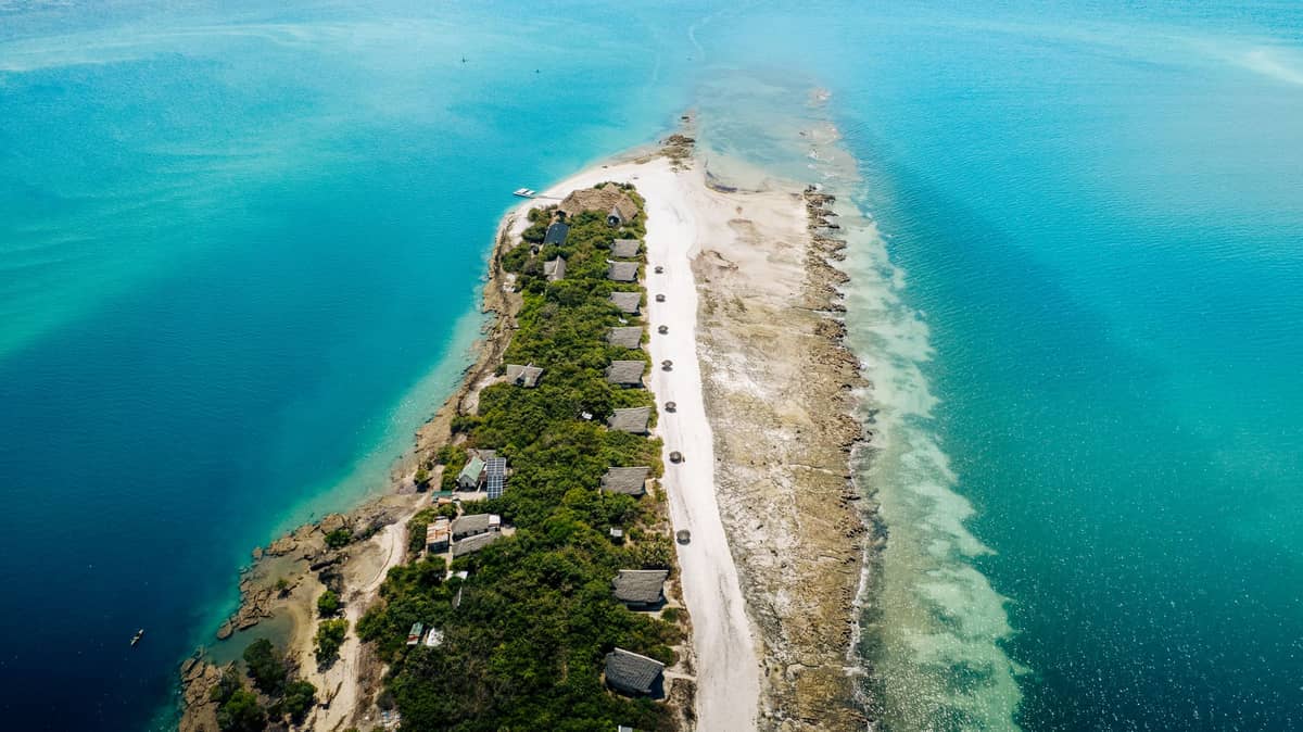 Luftaufnahme einer luxuriösen Privatinsel in Sansibar mit Strandvillen, umgeben von türkisblauem Wasser des Indischen Ozeans und üppigem Grün.
