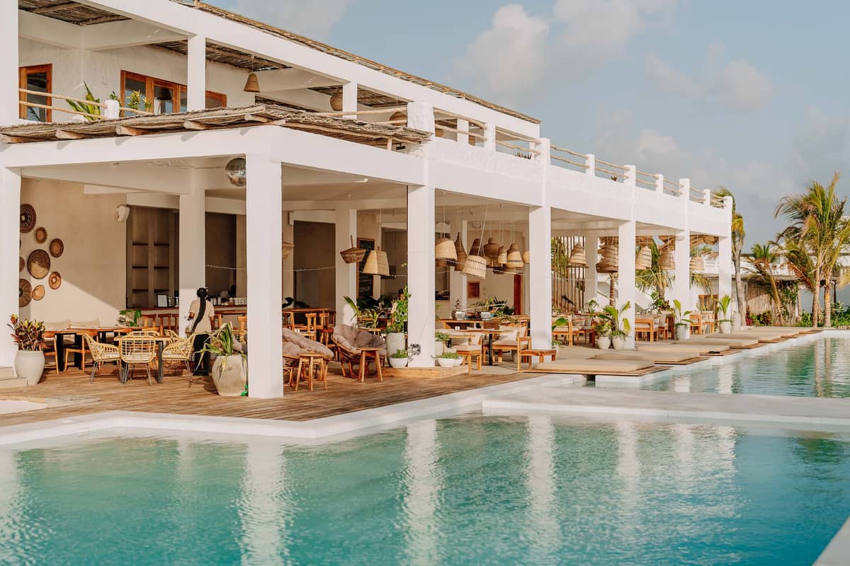 Luxuriöses Strandresort in Sansibar mit moderner weißer Architektur, Open-Air-Lounge-Bereichen, Pool, Palmen und dem im Hintergrund sichtbaren Ozean.