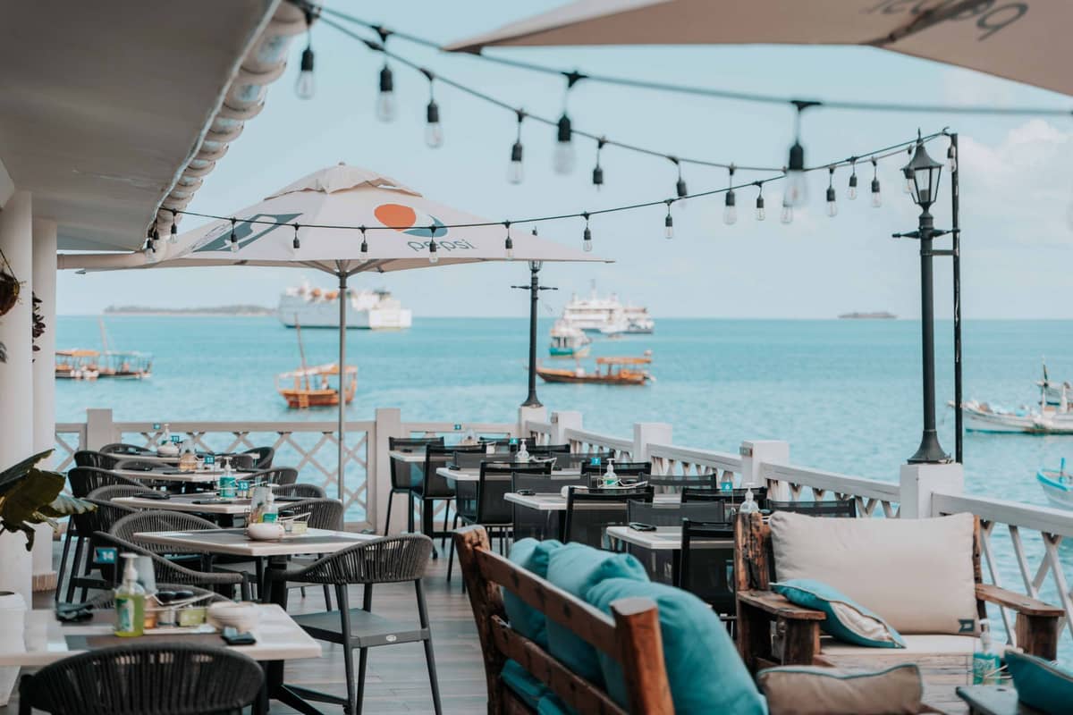 Nadmorski bar i taras restauracyjny na Zanzibarze z lampkami sznurkowymi, stolikami i łodziami na wodzie — zachęcająca atmosfera nocnego życia.