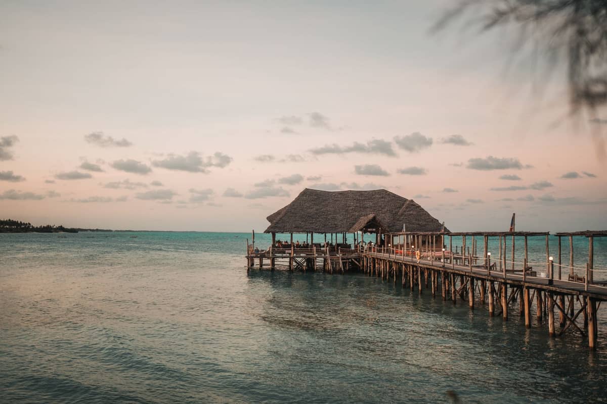 Muelle de madera con cabaña de techo de paja que se adentra en el agua turquesa al atardecer en una tranquila playa de Zanzibar.