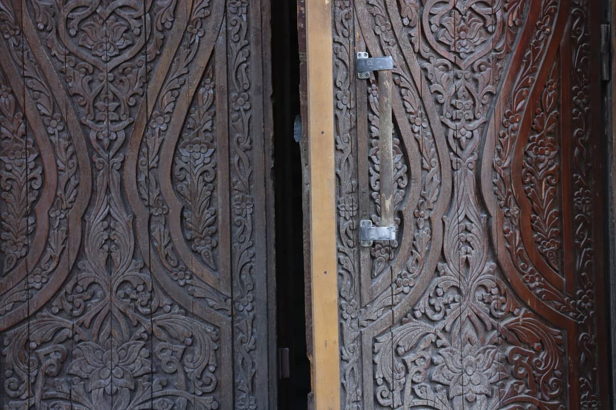 Close-up of a beautifully carved wooden double door with floral and organic patterns, partially open