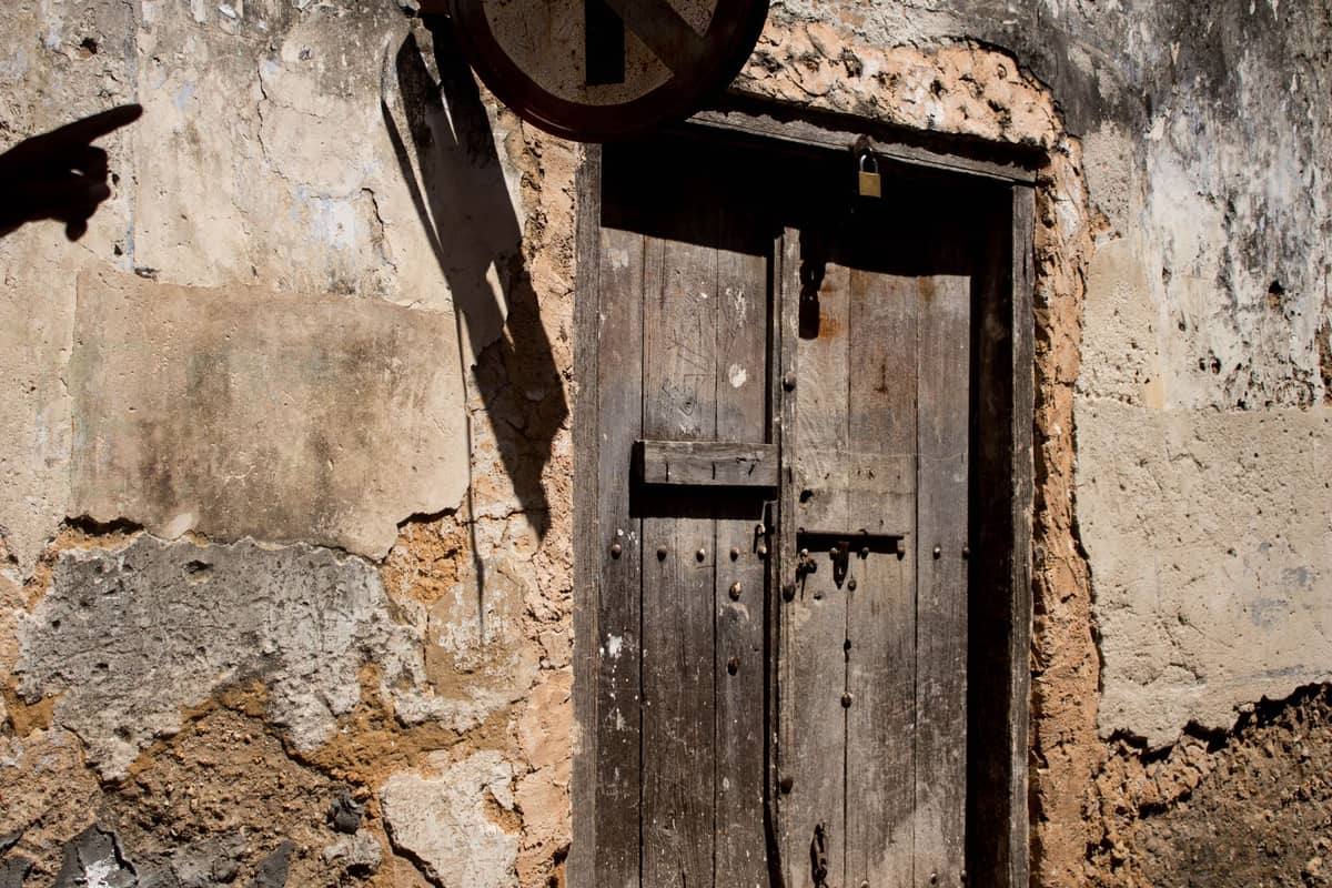Old stone wall with rough, pitted cream-to-ochre coral ragstone and a timber door, showing materials typical of Zanzibar’s Stone Town architecture.