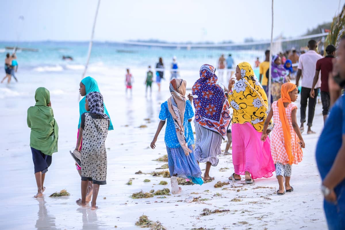 Kobiety i dziewczęta suahili w kolorowych tradycyjnych strojach spacerujące po plaży na Zanzibarze – codzienne życie nad morzem.