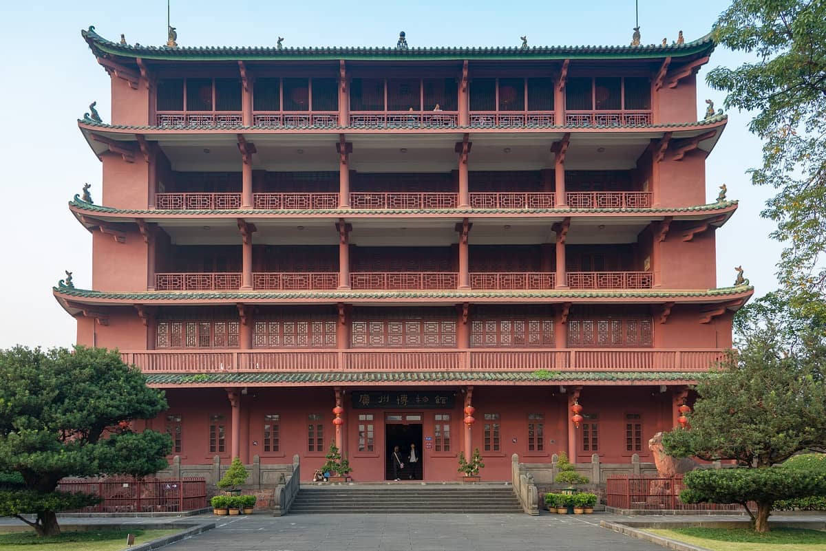 Front view of Zhenhai Tower, a five-story red historic building with green tiled roofs and traditional Chinese architectural details, surrounded by greenery.