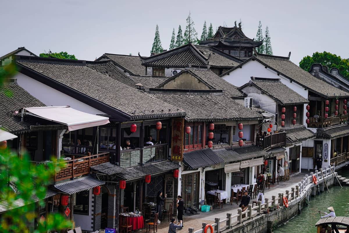 Historische Kanalhäuser mit grauen Ziegeldächern und roten Laternen entlang des Wasserwegs in Zhujiajiao, Shanghais alter Wasserstadt.