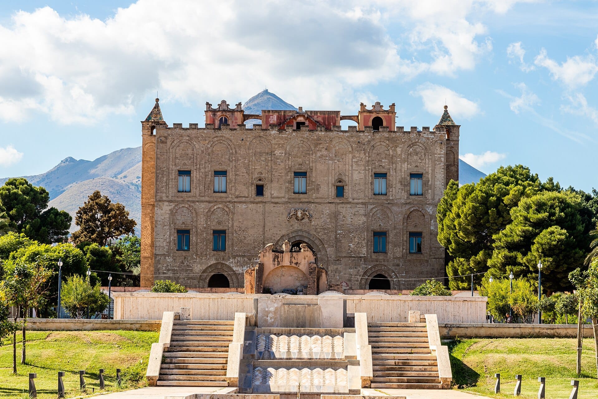 Frontansicht des Castello della Zisa in Palermo mit seiner markanten normannischen Architektur, großen Bogenfenstern und einer von Grünflächen umgebenen Steintreppe.