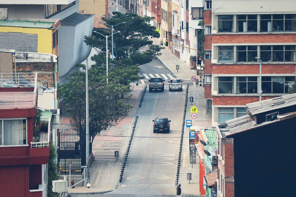 A narrow street in Bogotá's Chapinero neighborhood flanked by low-rise buildings, some with brick facades, and a few cars driving along the road.