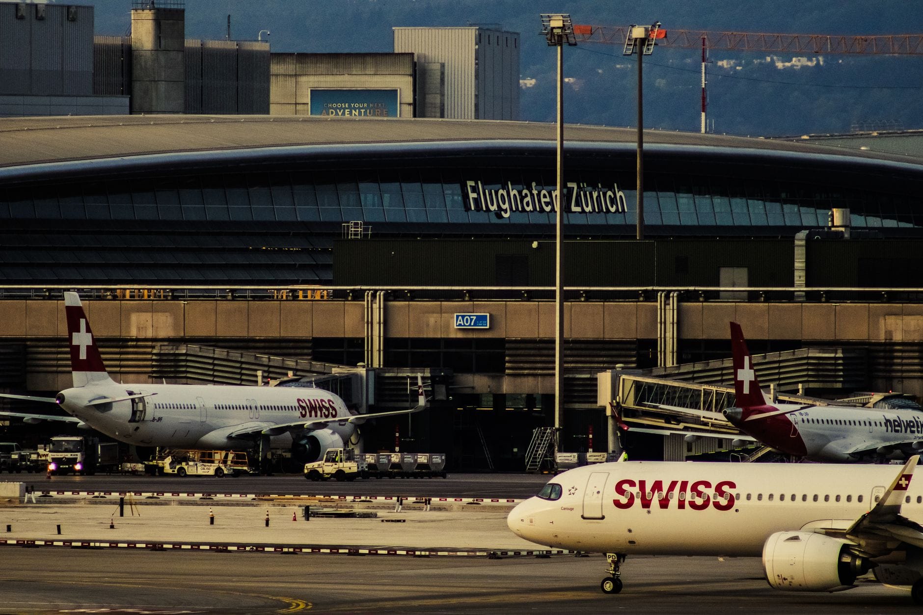 วิวเทอร์มินัลสนามบินซูริก เห็นเครื่องบิน Swiss และป้าย 'Flughafen Zürich' ชัดเจน แสดงบรรยากาศเทอร์มินัลและกิจกรรมสนามบิน