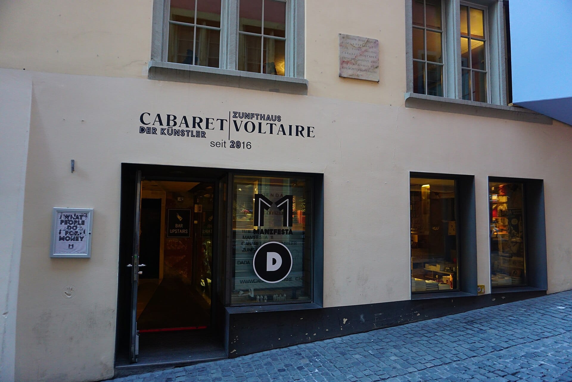 มุมถนนหน้าทางเข้า Cabaret Voltaire ในซูริก เห็นป้ายและหน้าต่างร้านริมตรอกหินโบราณในย่าน Niederdorf
