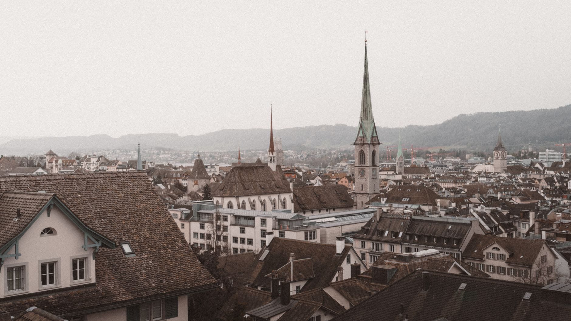 วิวฤดูหนาวที่ครึ้มฟ้าครึ้มฝนของหลังคาและยอดโบสถ์ใน Altstadt ของซูริกภายใต้ท้องฟ้าสีเทา อันเป็นลักษณะทั่วไปของสภาพอากาศเดือนธันวาคมในเมืองนี้