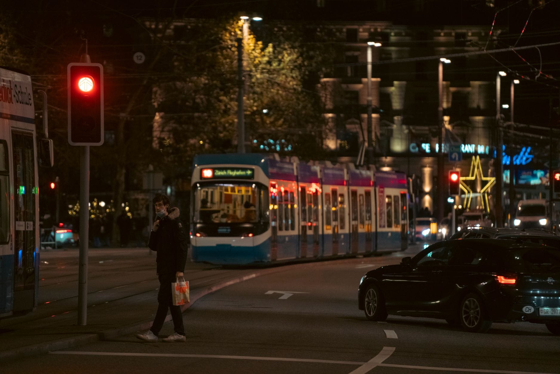 รถรางในเมือง Zurich ยามค่ำคืน พร้อมผู้โดยสาร ไฟถนน รถยนต์ และคนเดินเท้าข้ามทางแยกในเมือง