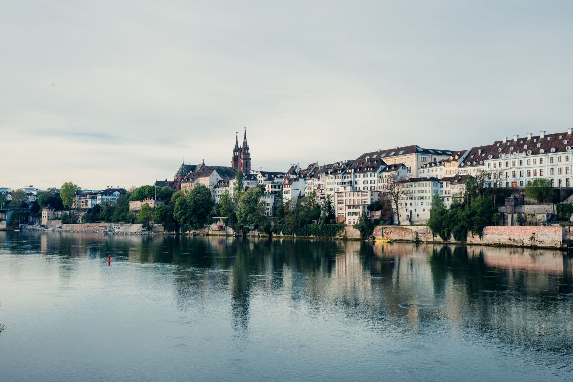 วิวเมือง Basel พร้อมแม่น้ำ Rhine อาคารประวัติศาสตร์เรียงรายตามริมฝั่ง และมหาวิหาร Basler Münster ที่มองเห็นได้ในพื้นหลัง